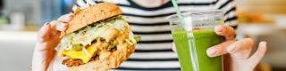 A young woman drinks green smoothies and eats a burger in a vegan fast food restaurant